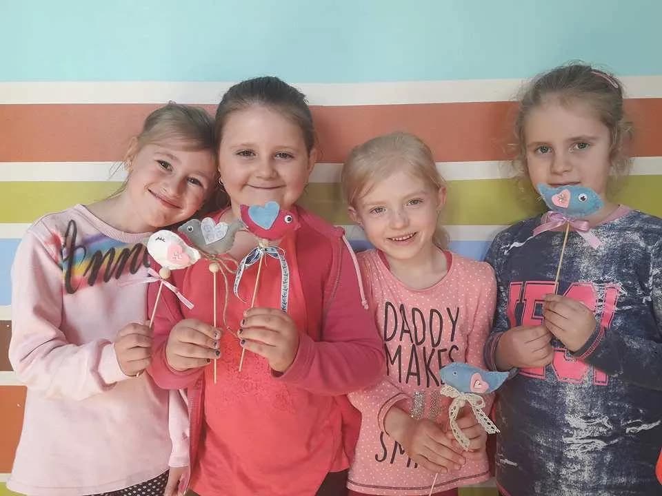 Zdjęcie przedstawia dzieci z placówki na tle ściany z kolorowymi paskami, które trzymają ozdoby na cienkich patyczkach.
