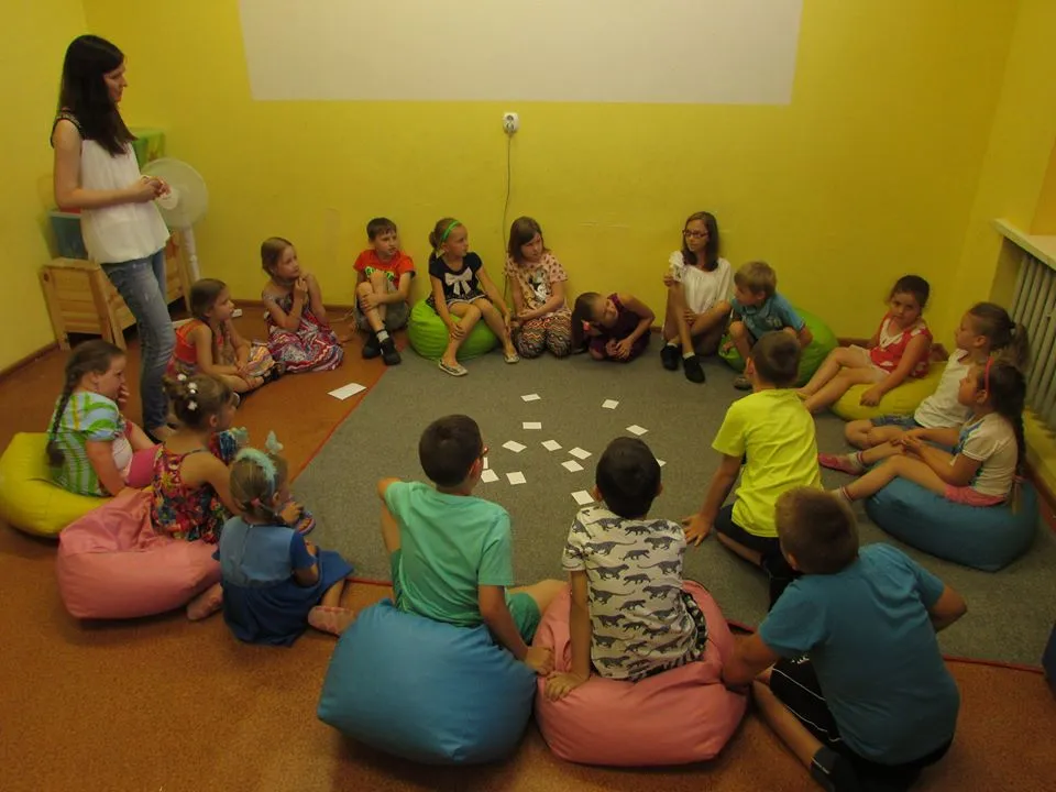 Zdjęcie przedstawia dzieci z placówki siedzących w okręgu podczas zajęć w sali z zielonymi ścianami.