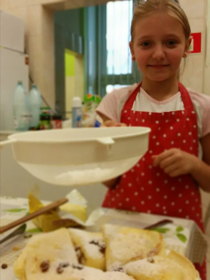 Zdjęcie przedstawia dziewczynkę z placówki kończącą dekorację ciasta.