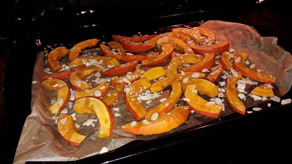 Obraz przedstawia kawałki dyni z miodem i migdałami w piekarniku.