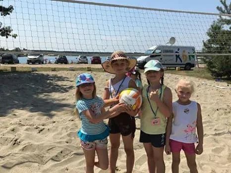 Na zdjęciu widnieją 4 dziewczynki trzymające piłkę do siatkówki na piaskowym boisku do siatkówki.