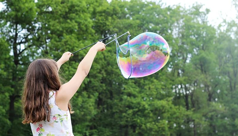 Dziecko na tle drzew puszczające bańkę mydlaną