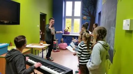 Zdjęcie przedstawia dzieci uczestniczące w warsztatach wokalnych w placówce wraz z instruktorem.