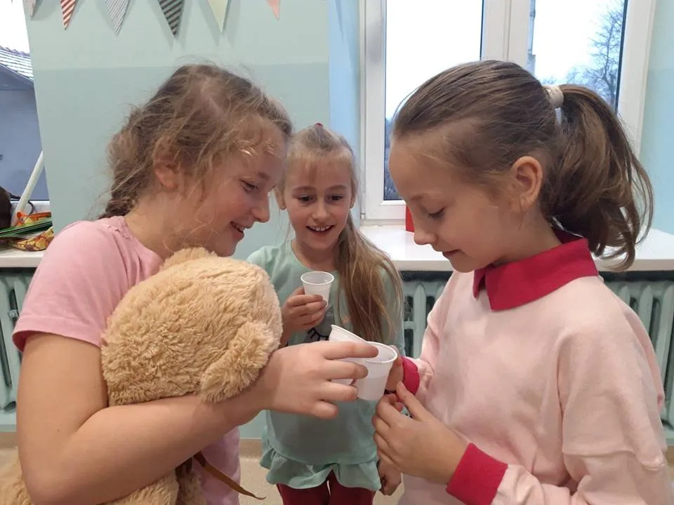 Obraz przedstawia dzieci pijące z kubeczków podczas światowego dnia życzliwości.