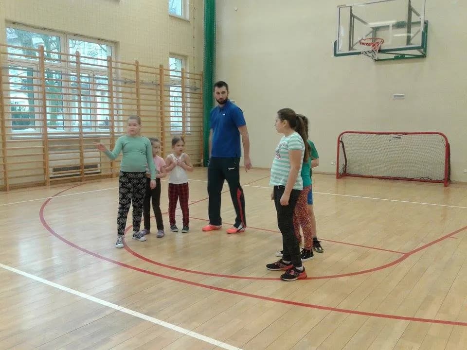 Zdjęcie przedstawia szóstkę dzieci z placówki oraz trenera na dużej sali gimnastycznej.